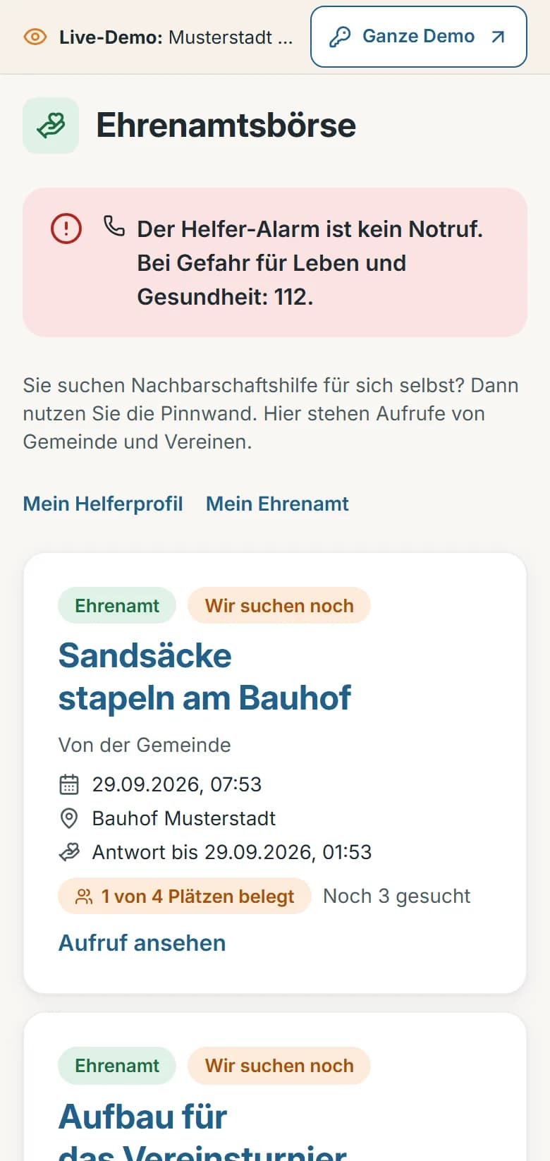 Ehrenamtsbörse der Demo-Gemeinde Musterstadt: Hinweis „Der Helfer-Alarm ist kein Notruf“, Aufruf der Gemeinde „Sandsäcke stapeln am Bauhof“ mit belegten Plätzen und darunter der Aufruf des Vereins „Aufbau für das Vereinsturnier“